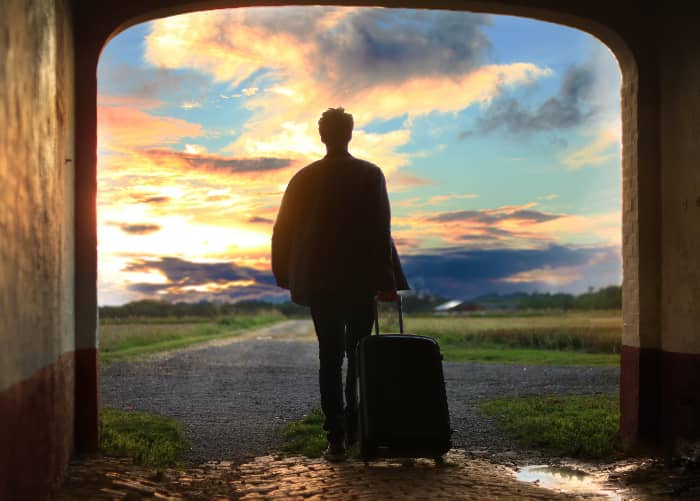 woman holding a suitcase walking into a sunset